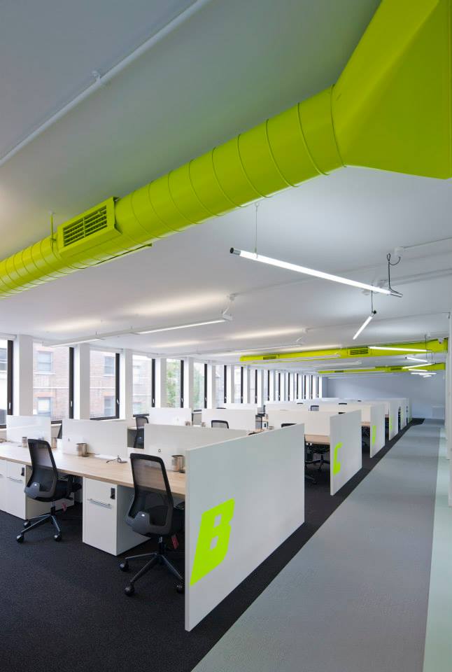Large open concept office with many white workstations and neon yellow paint accents