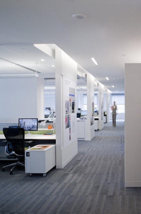 Workstations in the open concept office are given privacy by floor to-ceiling partition walls that are lit from above