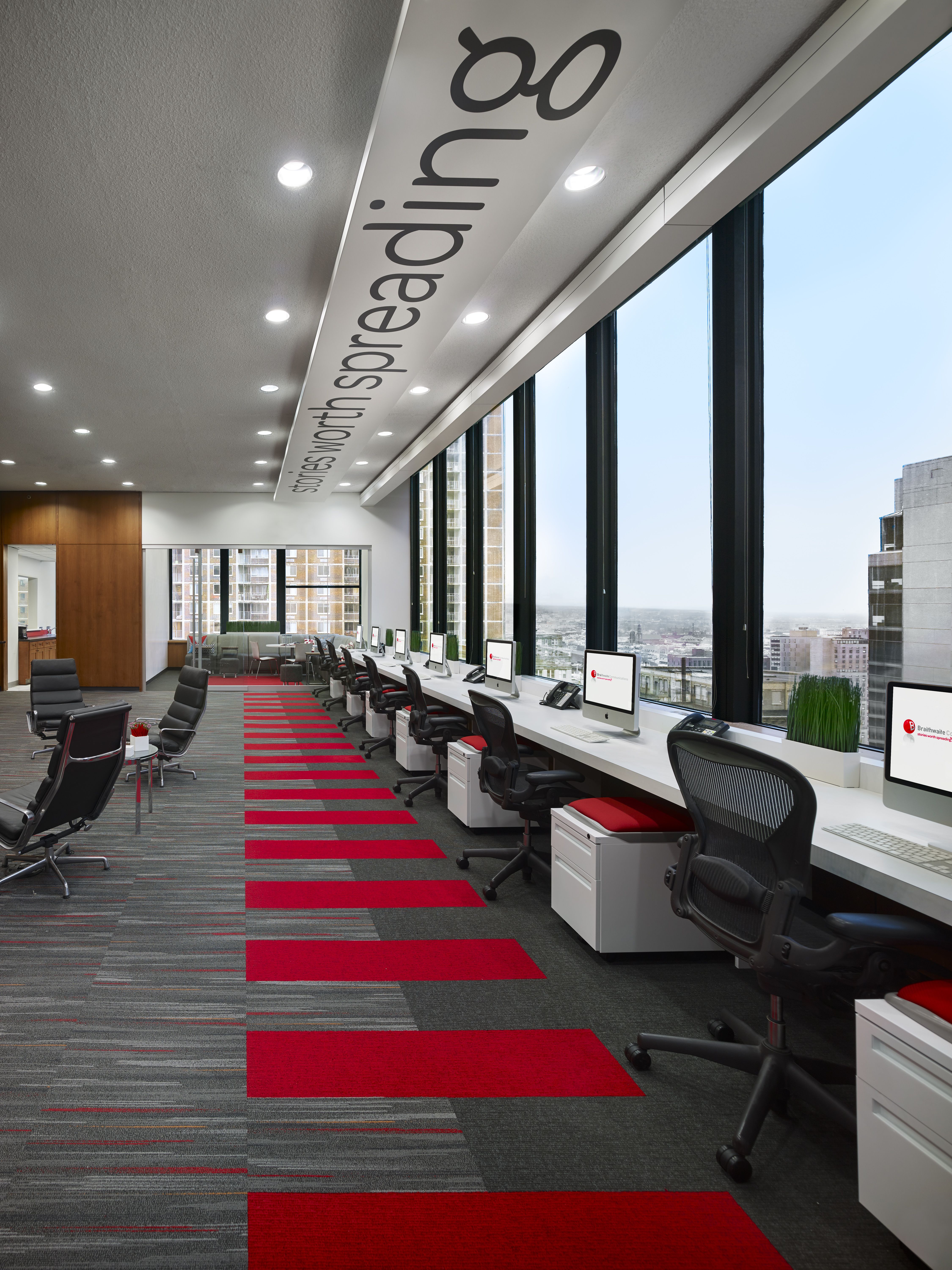 A long wall of bright modern workstations look out on floor to ceiling glass windows